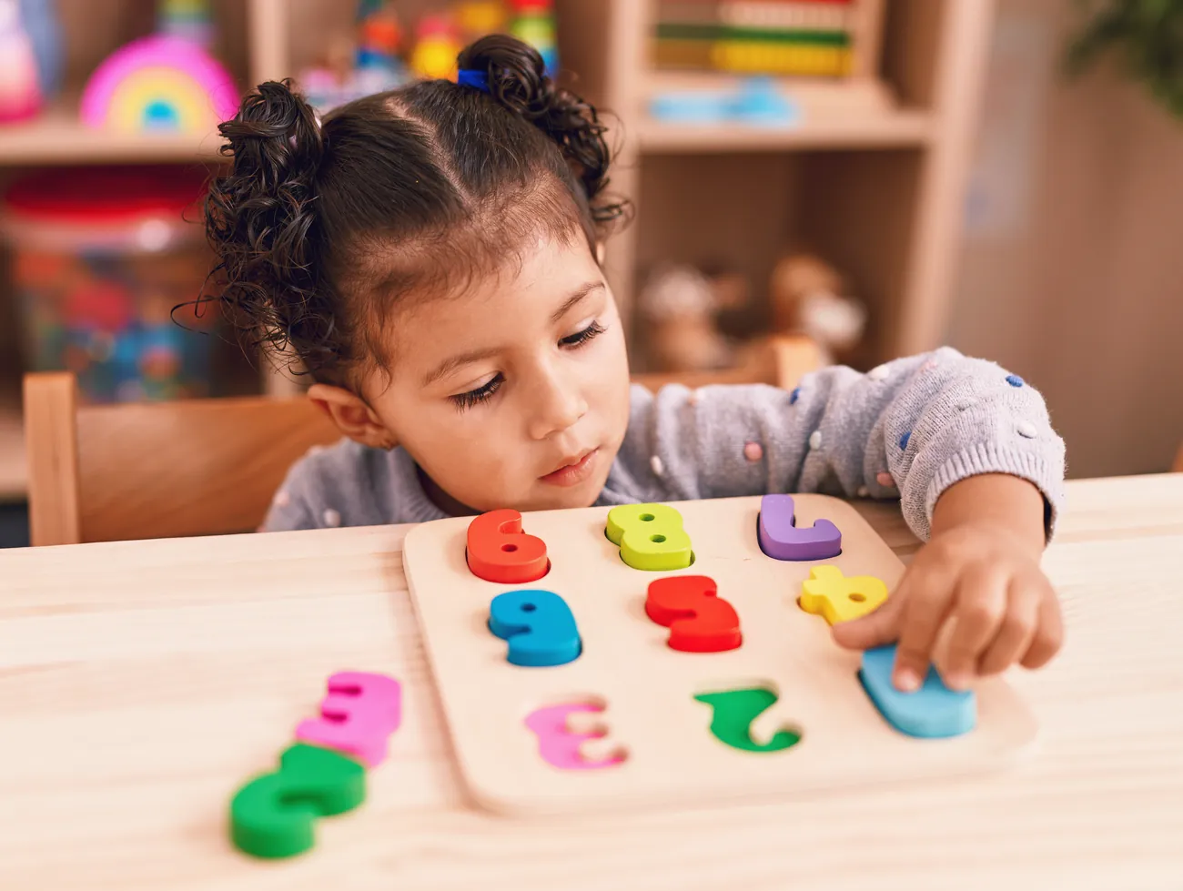 A young girl playing with a puzzle at a kindergarten table