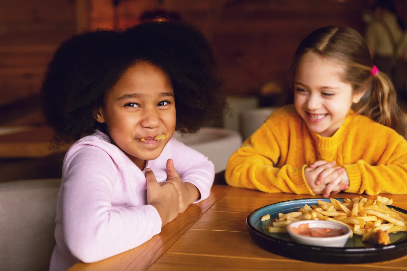 Two smiling girls sharing a plate of fries at a table