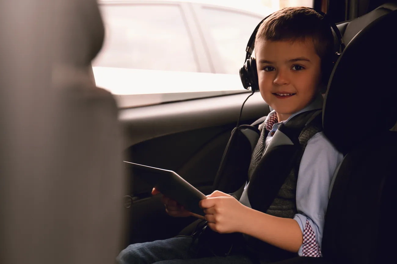 A little boy wearing headphones in the back seat of a car