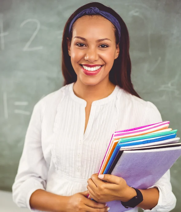 A teacher standing in front of a chalkboard holding a stack of books
