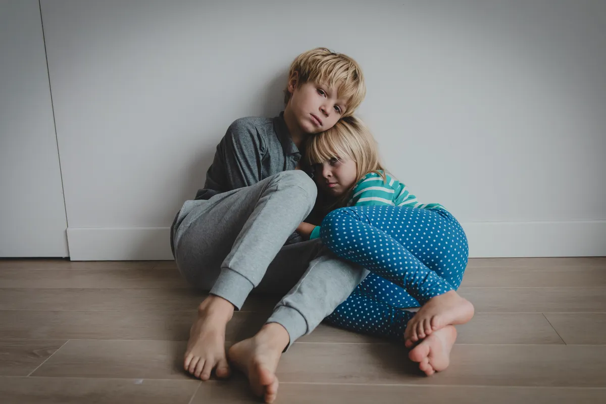 Two siblings sitting together on the floor at home